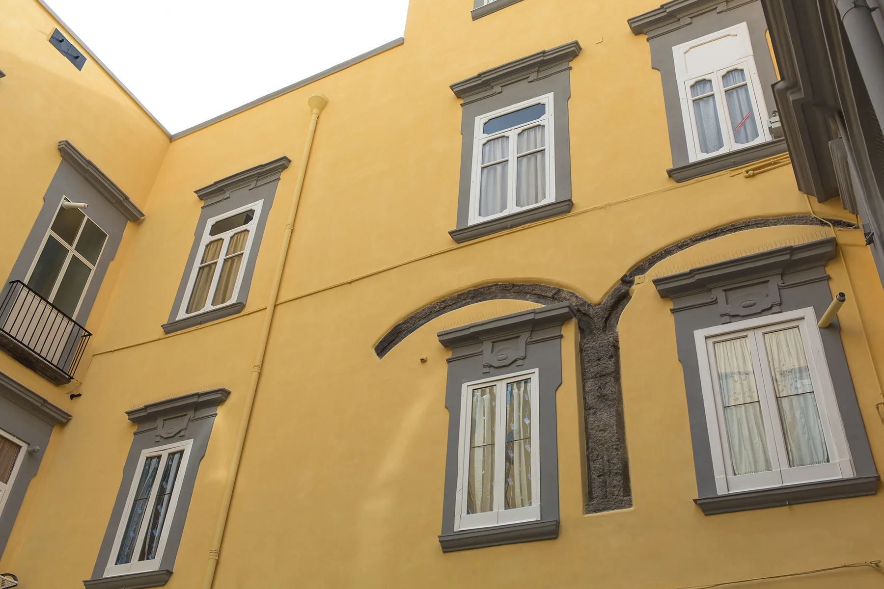 Paredes amarillas de un edificio con ventanas de marcos grises y molduras curvas.