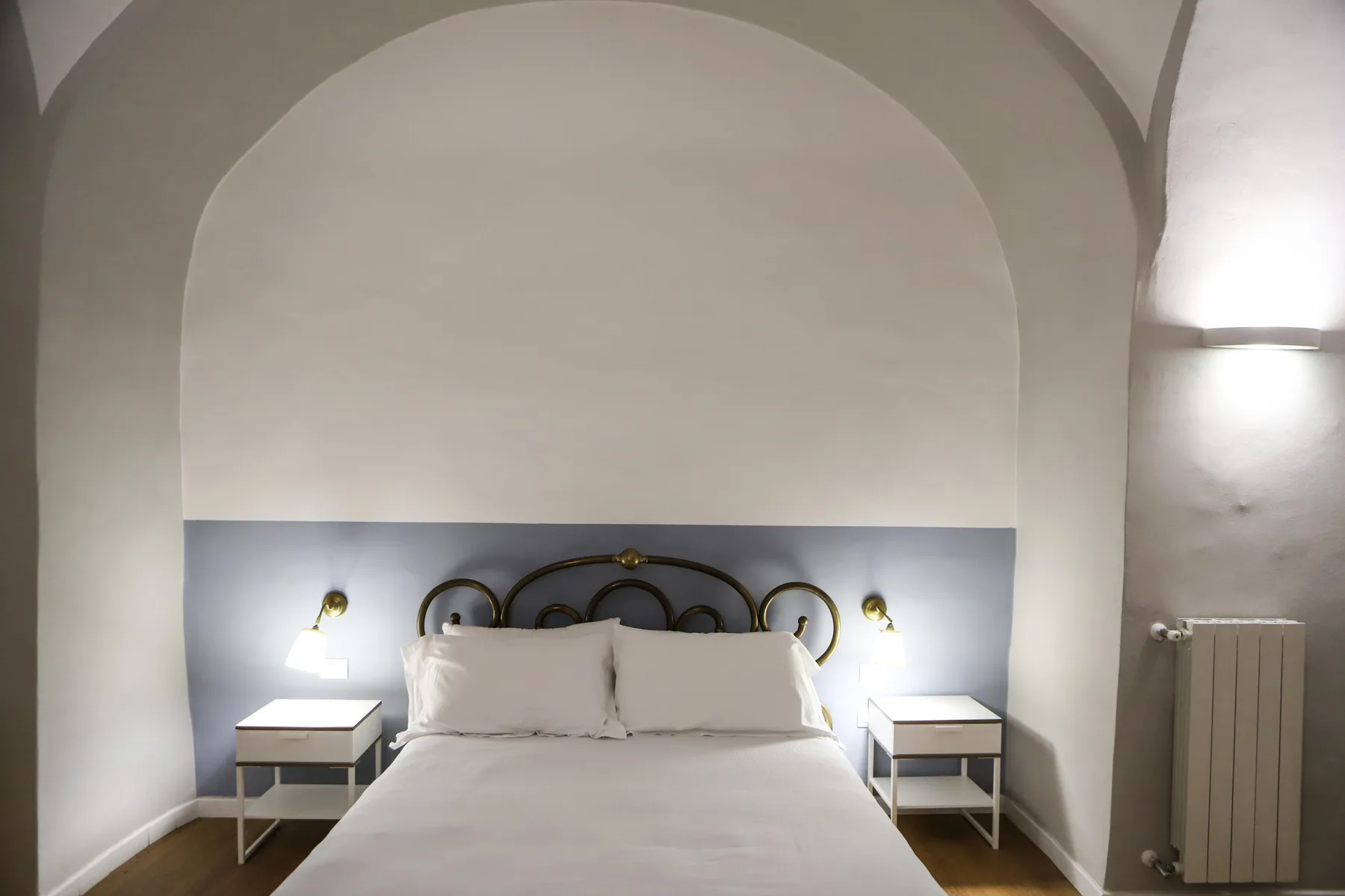 Un dormitorio con una cama entre dos mesitas de noche bajo una pared arqueada.