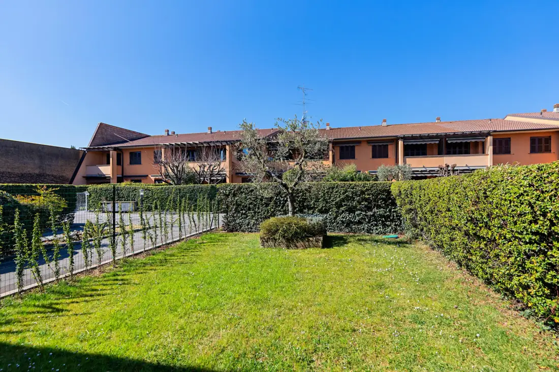 A grassy courtyard is bordered by hedges and an orange building.