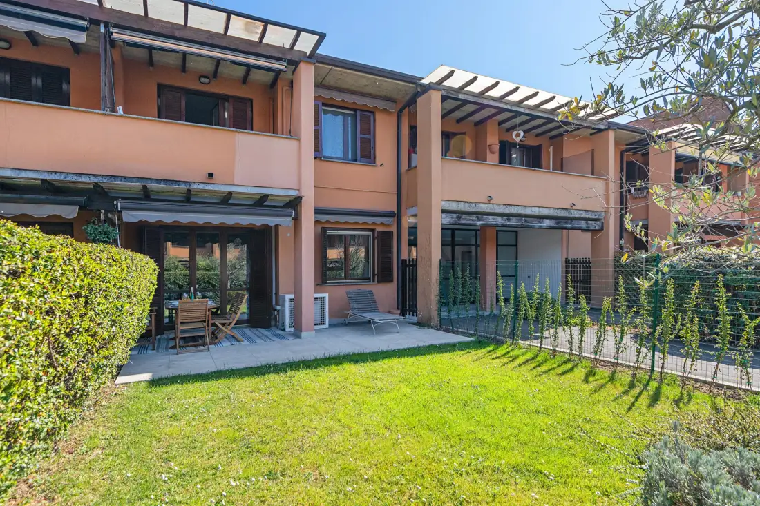 A two-story home faces a green lawn, with shaded patios and climbing plants.