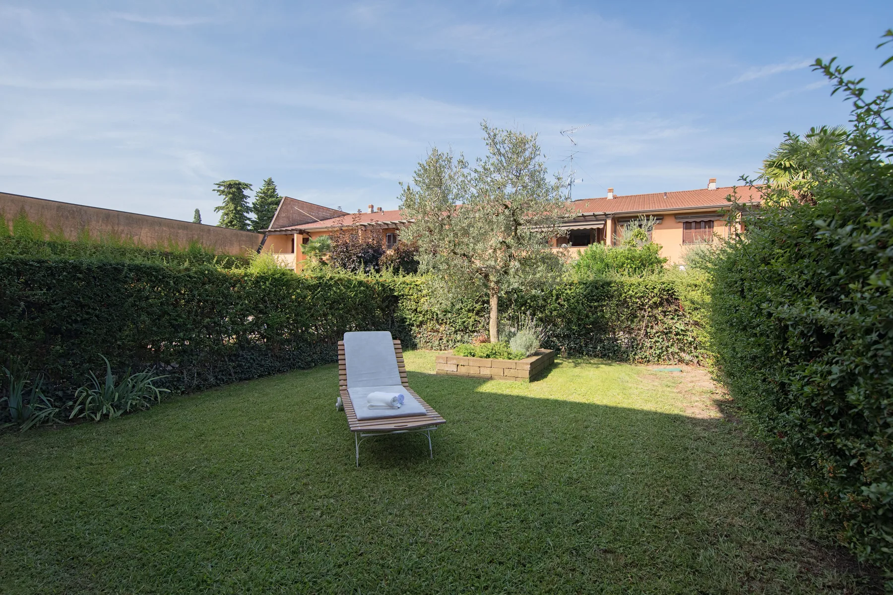A garden with a lawn, a reclining lounge chair, and hedges.