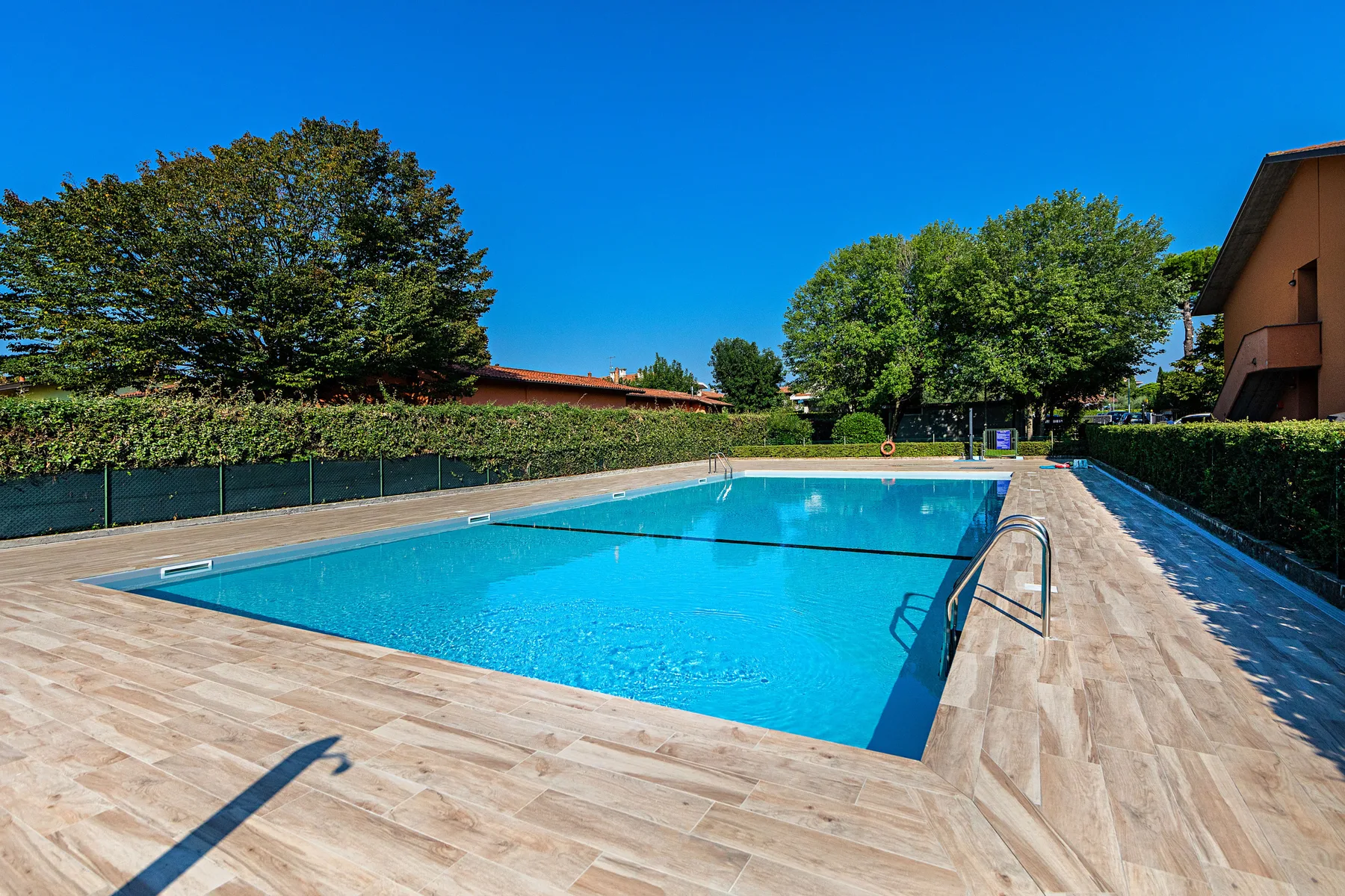 An outdoor swimming pool is surrounded by a paved deck and trees.