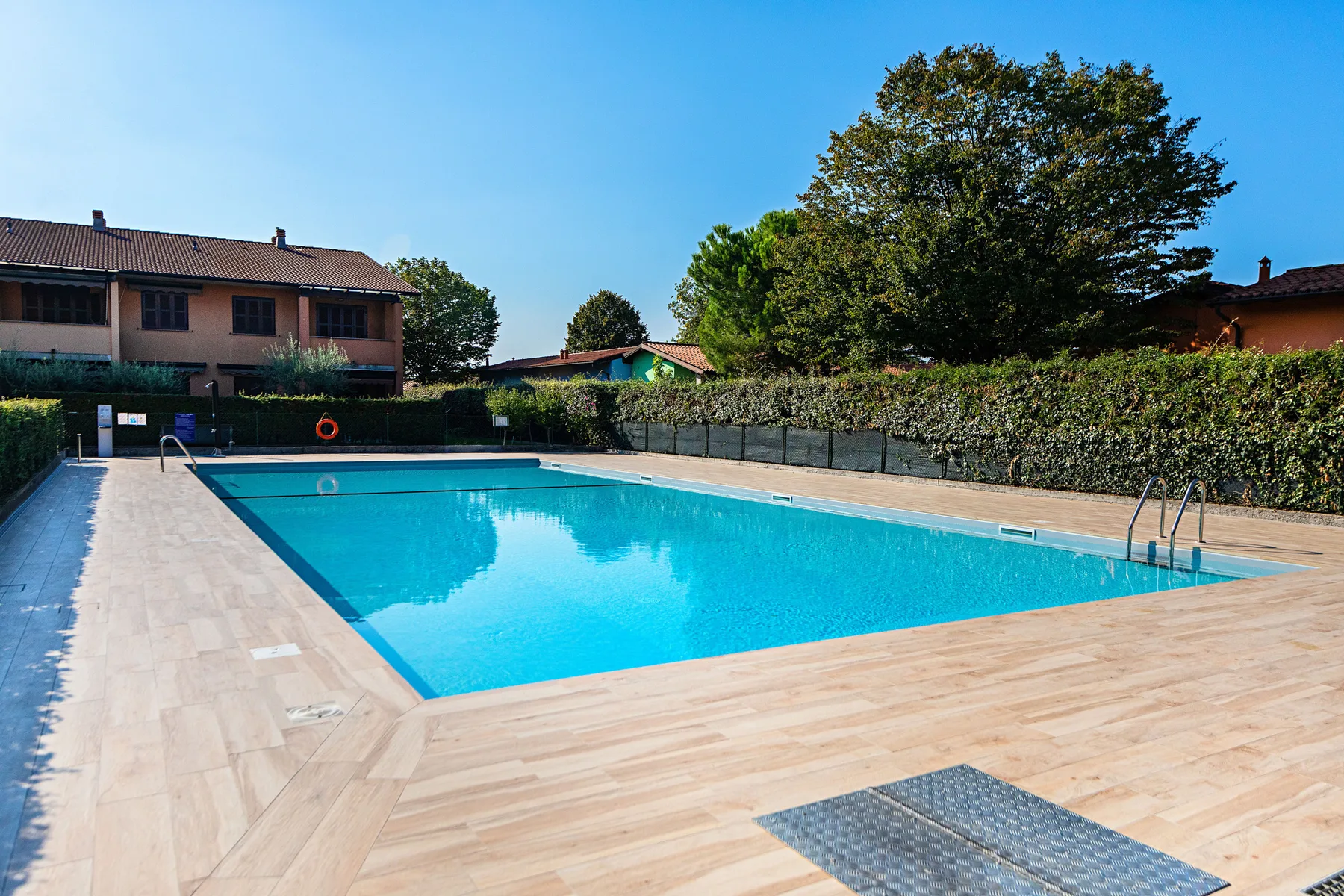 Outdoor swimming pool surrounded by a paved deck and greenery.