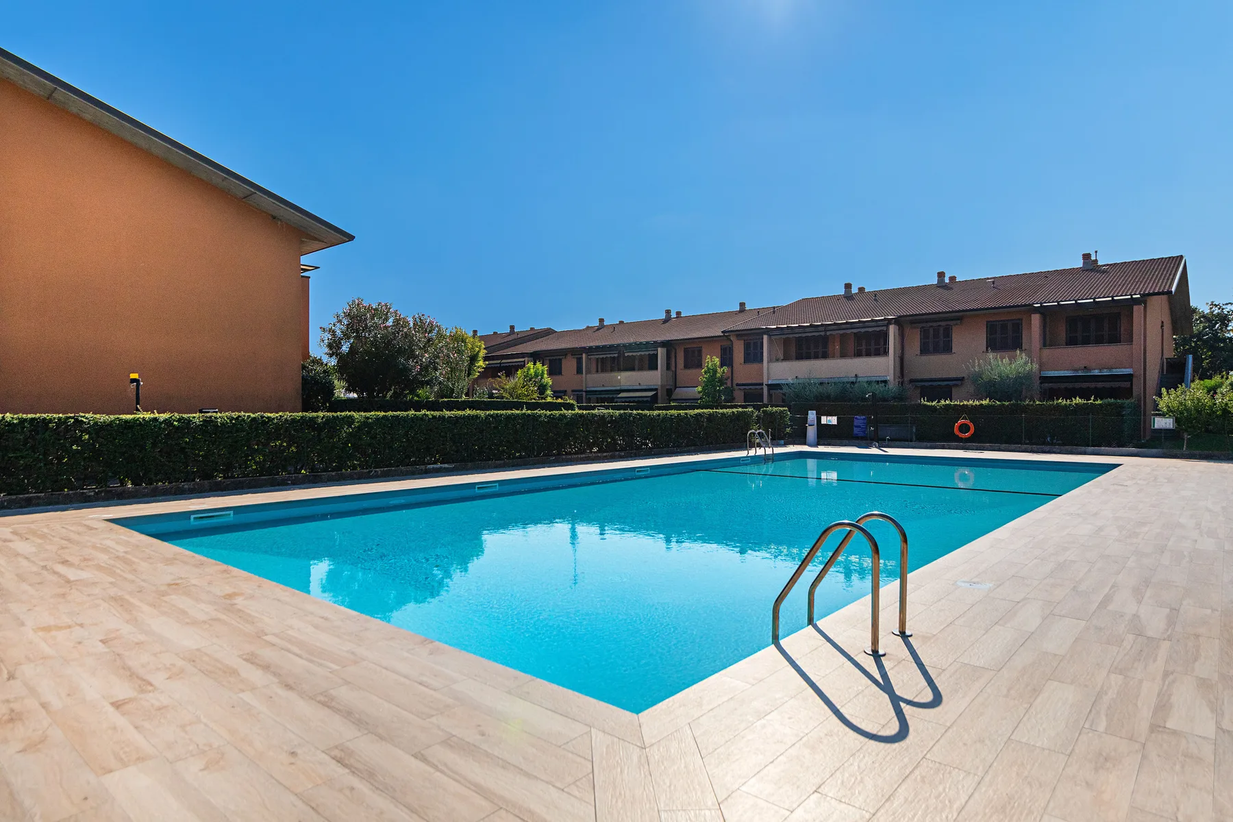 An outdoor swimming pool is surrounded by a paved deck and low buildings.