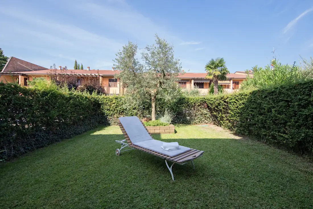 A grassy garden with a reclining lounge chair and tall hedges.