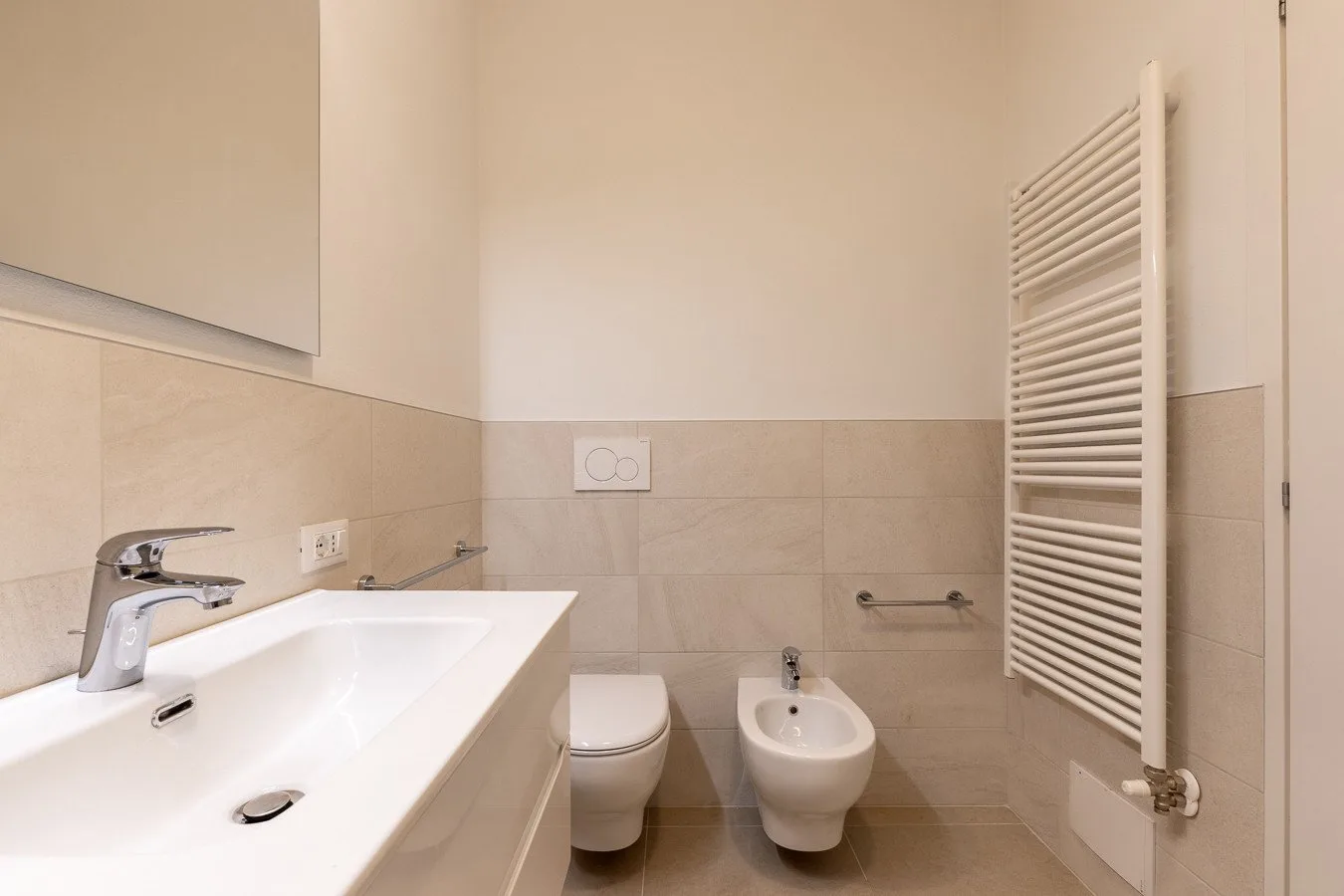 A bathroom with a sink, toilet, bidet, and wall-mounted towel radiator.