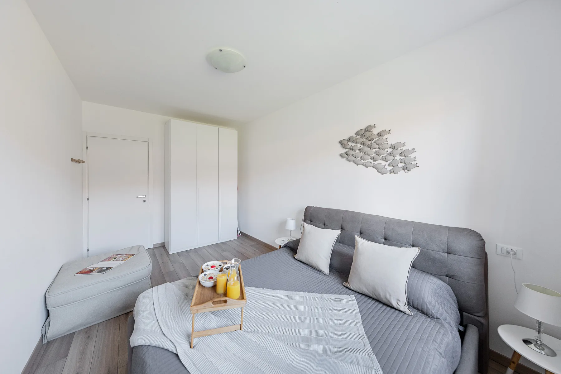 A bright bedroom with a gray bed, bedside table, and wall decoration.