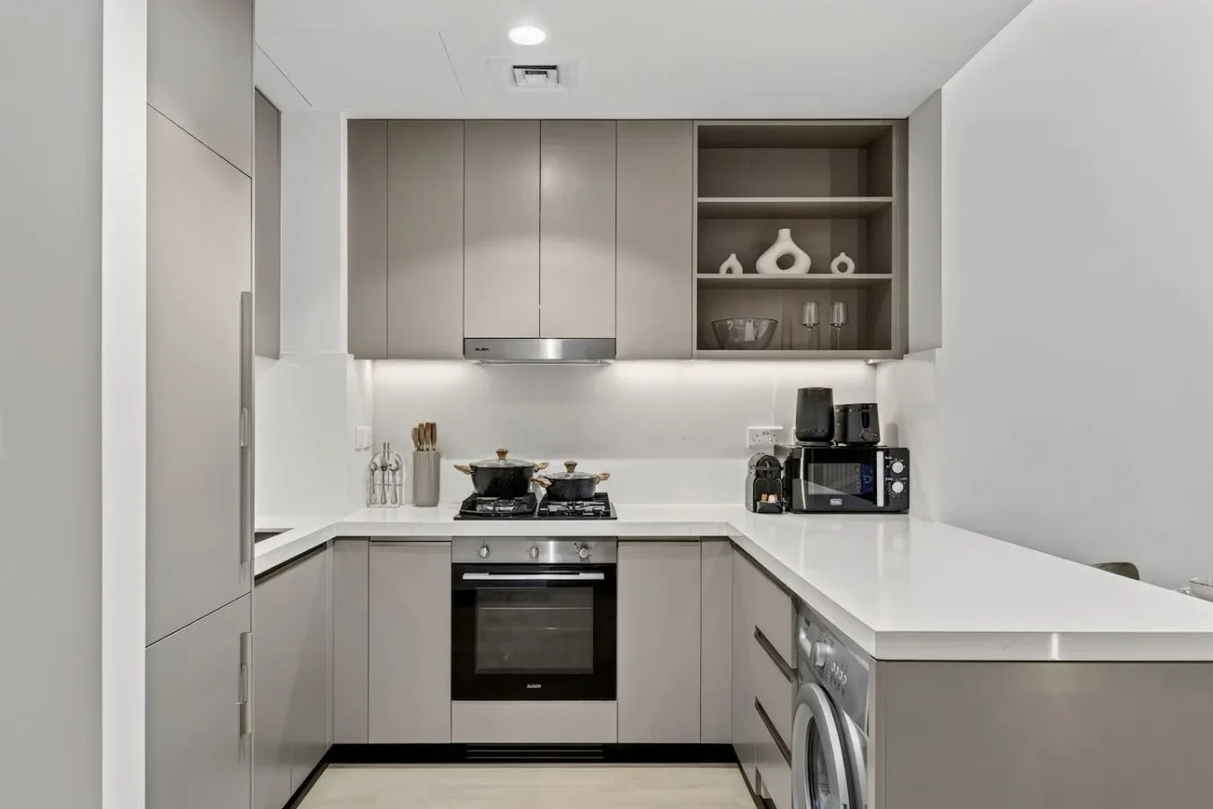 A modern kitchen with pale cabinets, a built-in oven, and a long white countertop.
