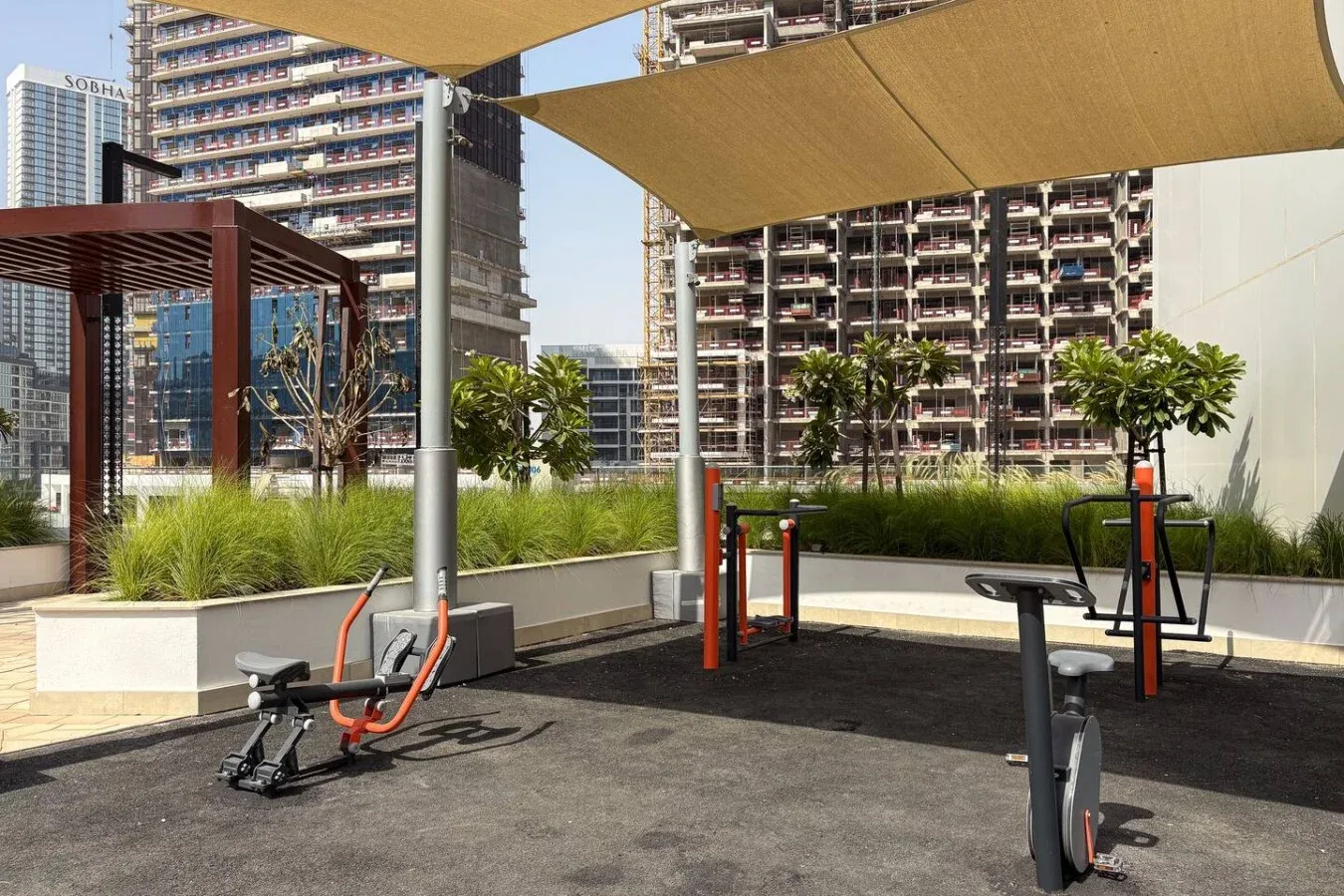 An outdoor exercise area with fitness equipment beneath shade sails.