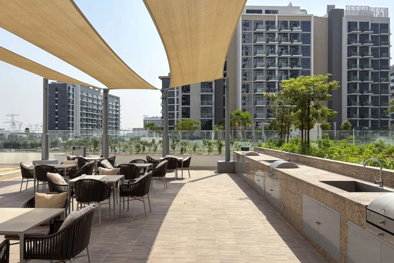 An outdoor terrace has seating beneath shade canopies, with apartment buildings in the background.