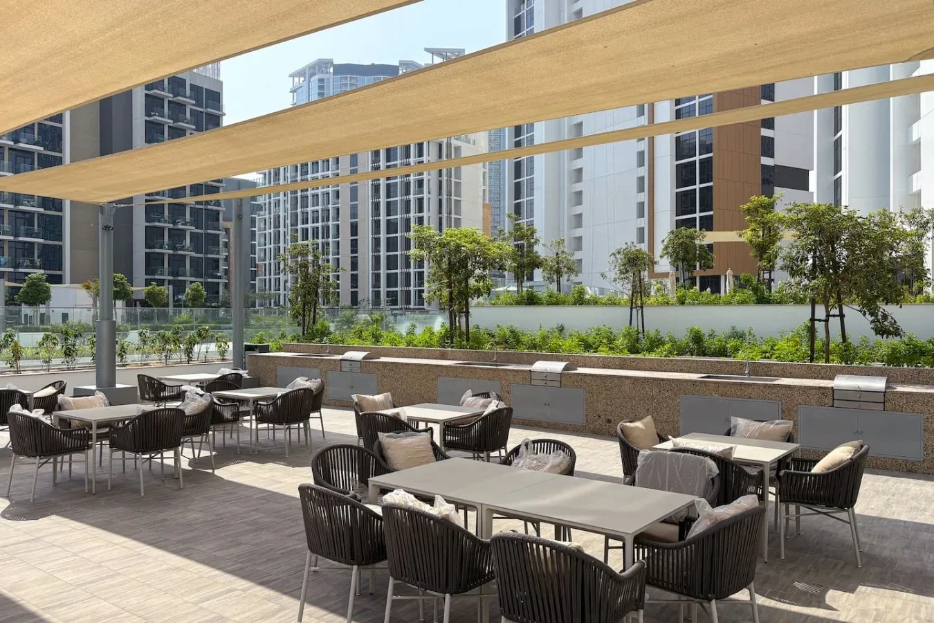 An outdoor dining terrace has tables and seating beneath broad shade canopies.