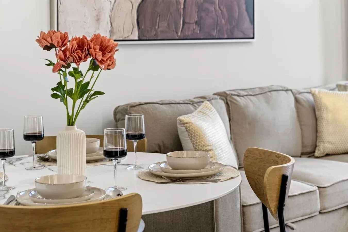 A dining table set with dishes and flowers sits beside a living room sofa.
