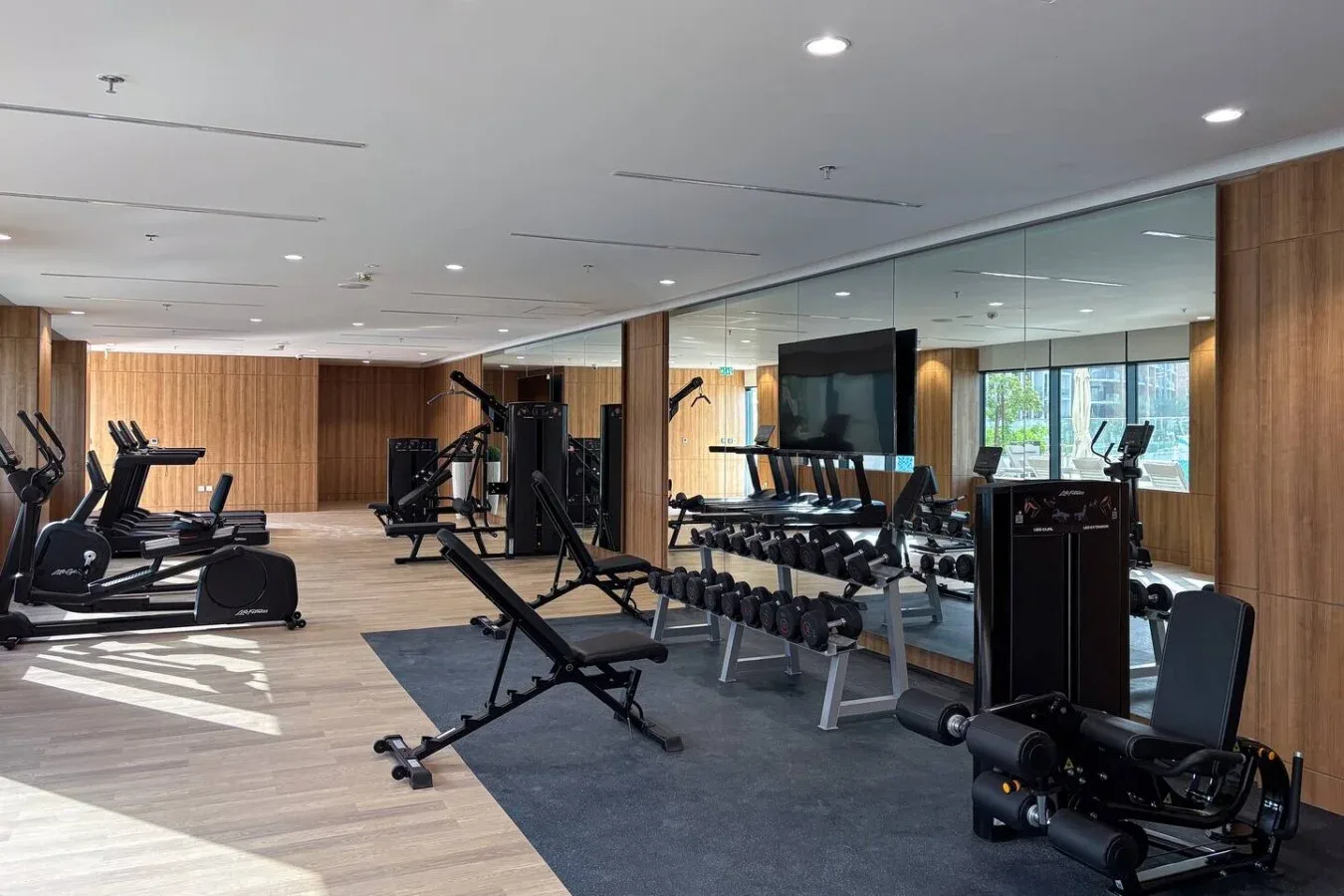 A fitness room with exercise machines and a row of dumbbells beside a mirrored wall.