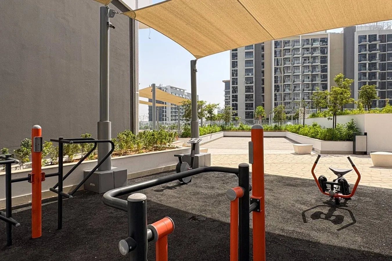 An outdoor fitness area with exercise equipment beneath a shade canopy.