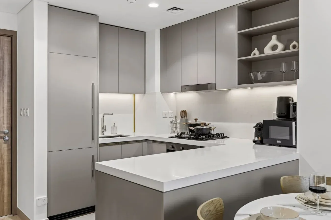A modern kitchen with gray cabinets, white countertops, and a dining area.