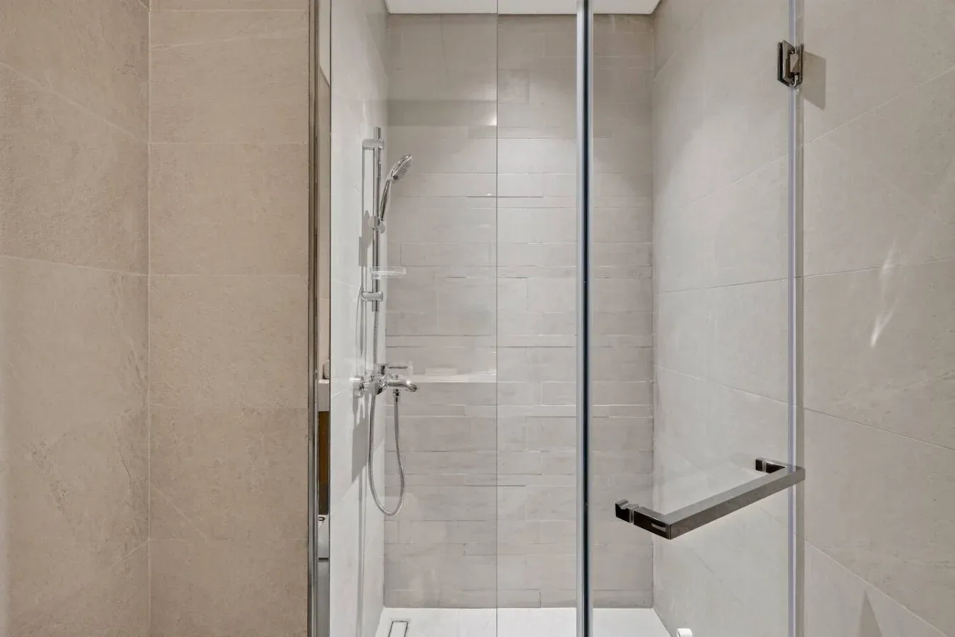 A tiled bathroom shower with a handheld showerhead and glass panels.