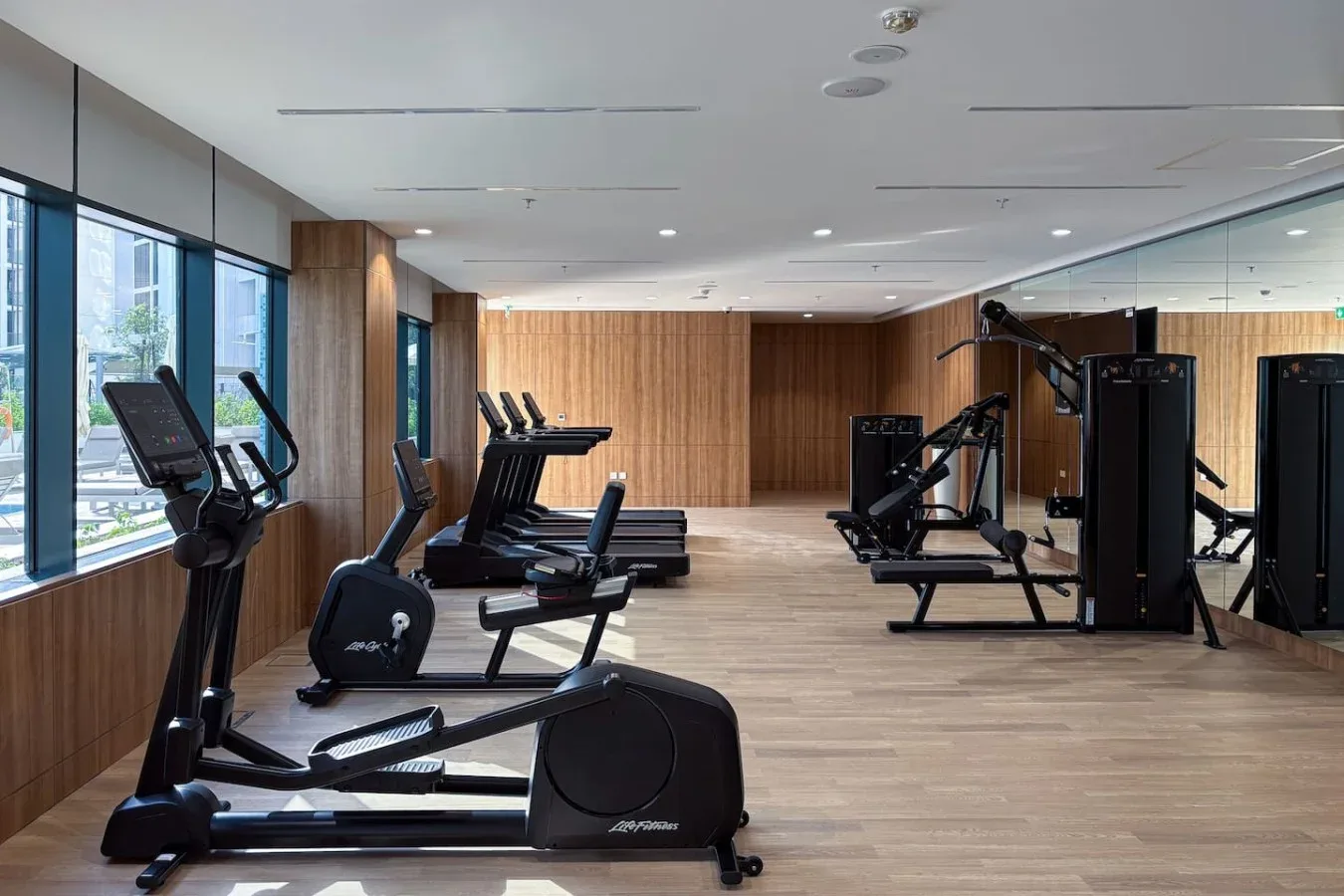 A gym with exercise machines arranged beside large windows and mirrored walls.