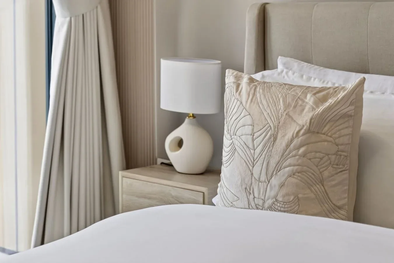 A neatly made bedroom with a bedside lamp and decorative pillows.