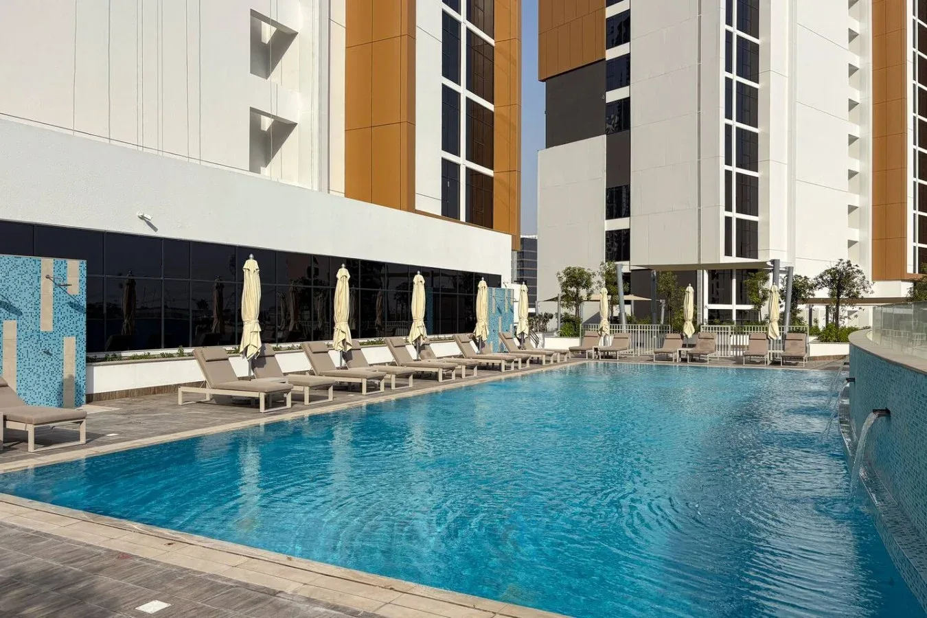 An outdoor swimming pool beside a modern building, with loungers along the edge.
