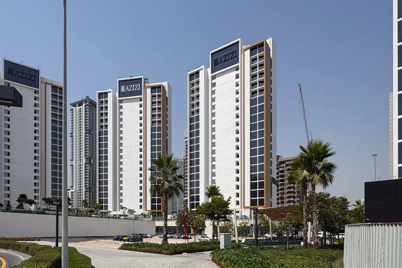 Modern high-rise buildings stand behind landscaped grounds with palm trees.