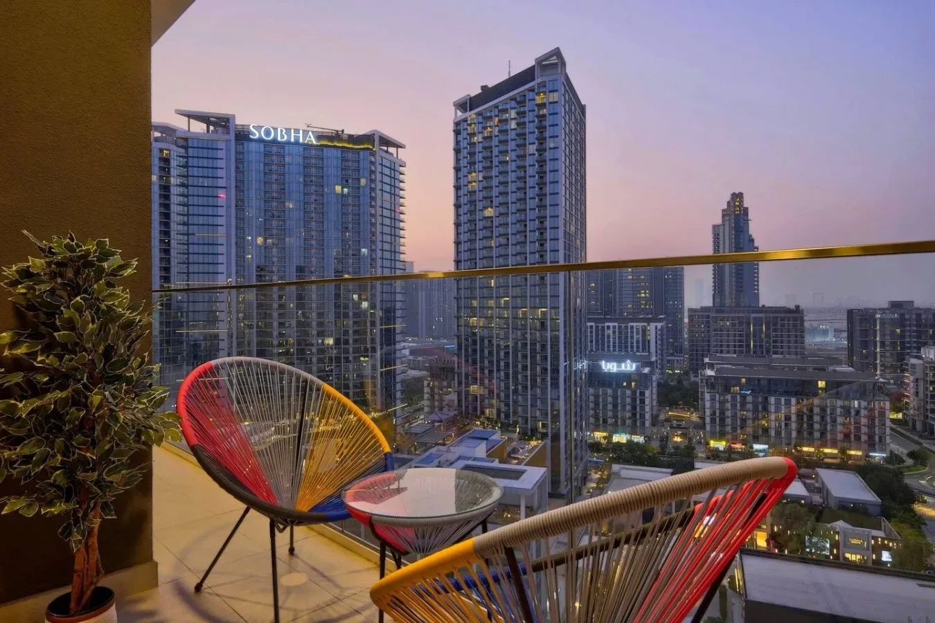 A balcony seating area overlooks illuminated city buildings at dusk.