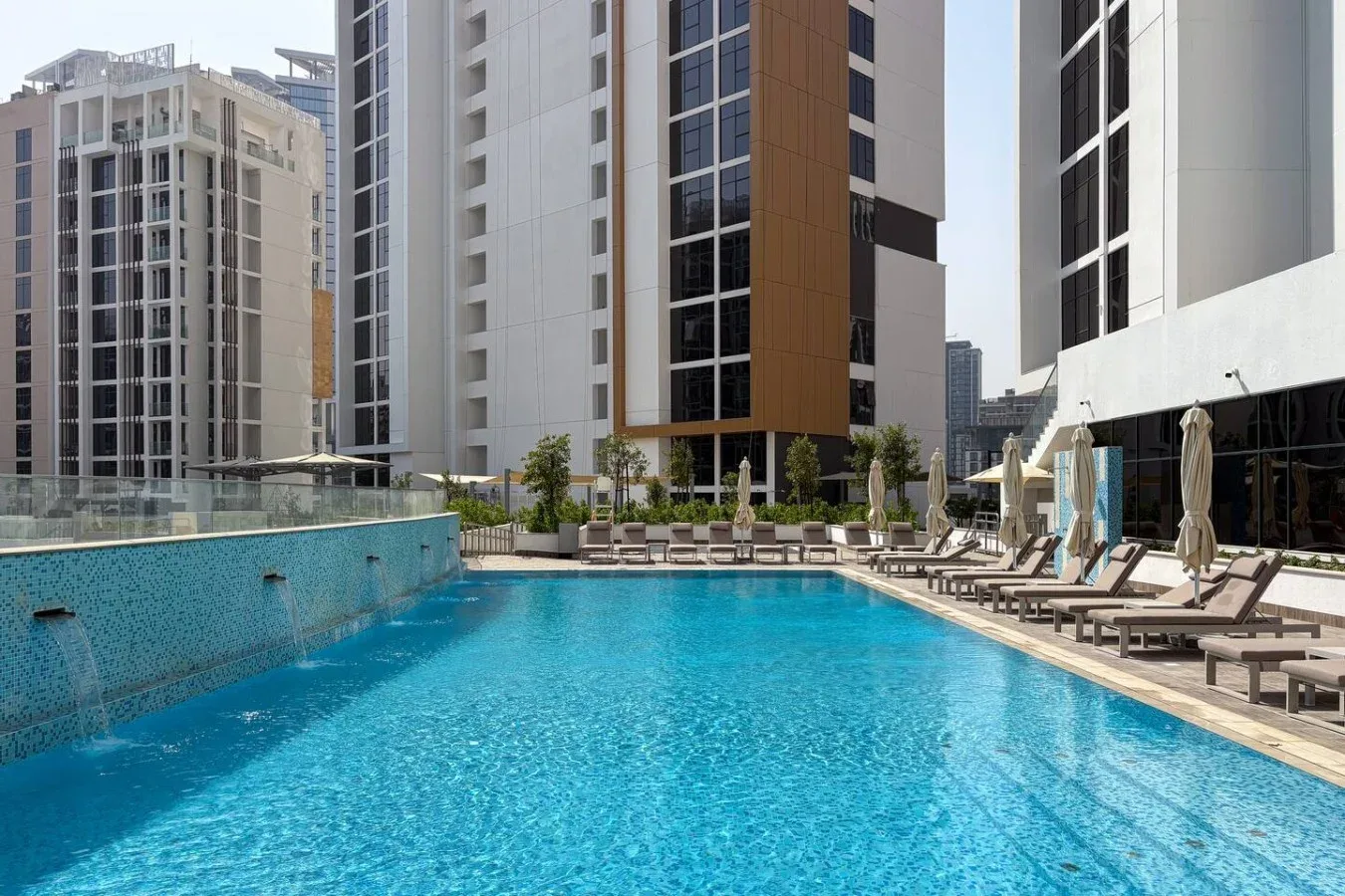 An outdoor swimming pool with lounge chairs beside modern high-rise buildings.