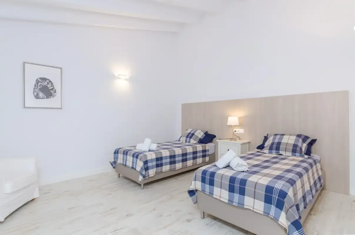 A bright bedroom with two beds dressed in blue plaid bedding.