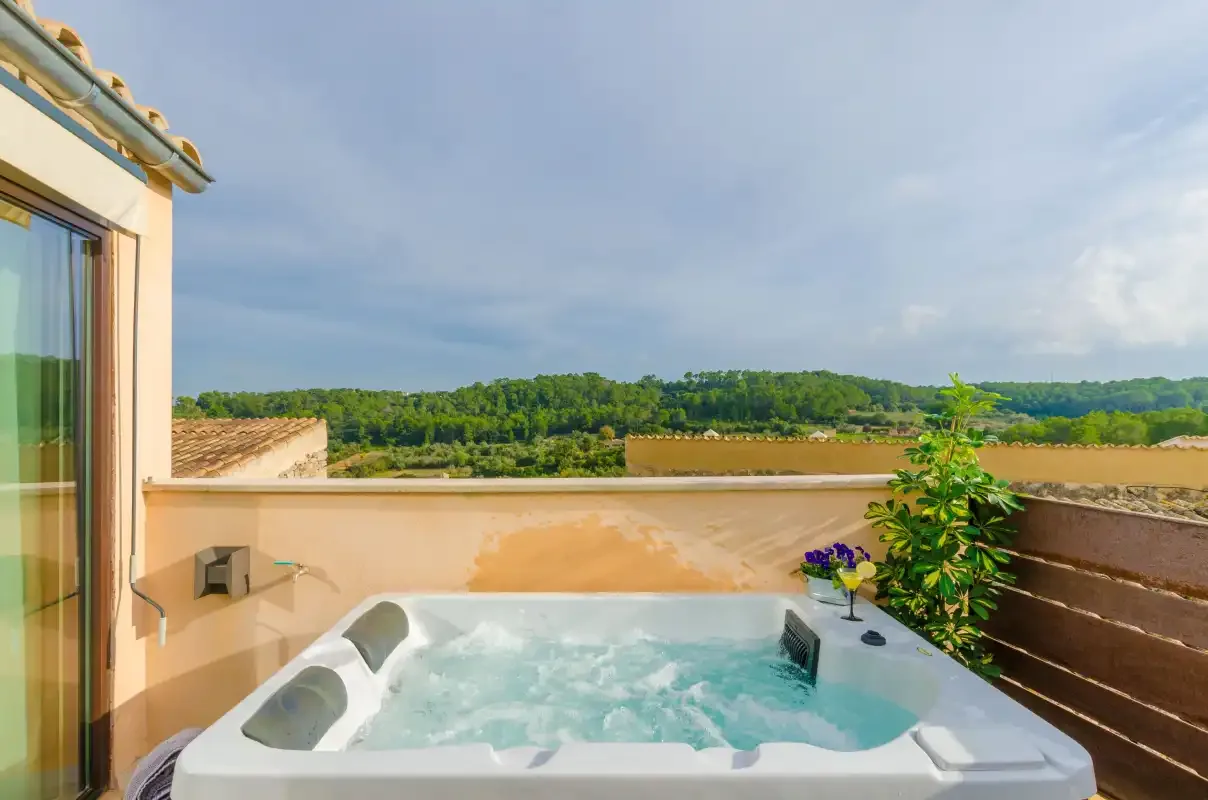 An outdoor hot tub sits on a terrace overlooking green hills.