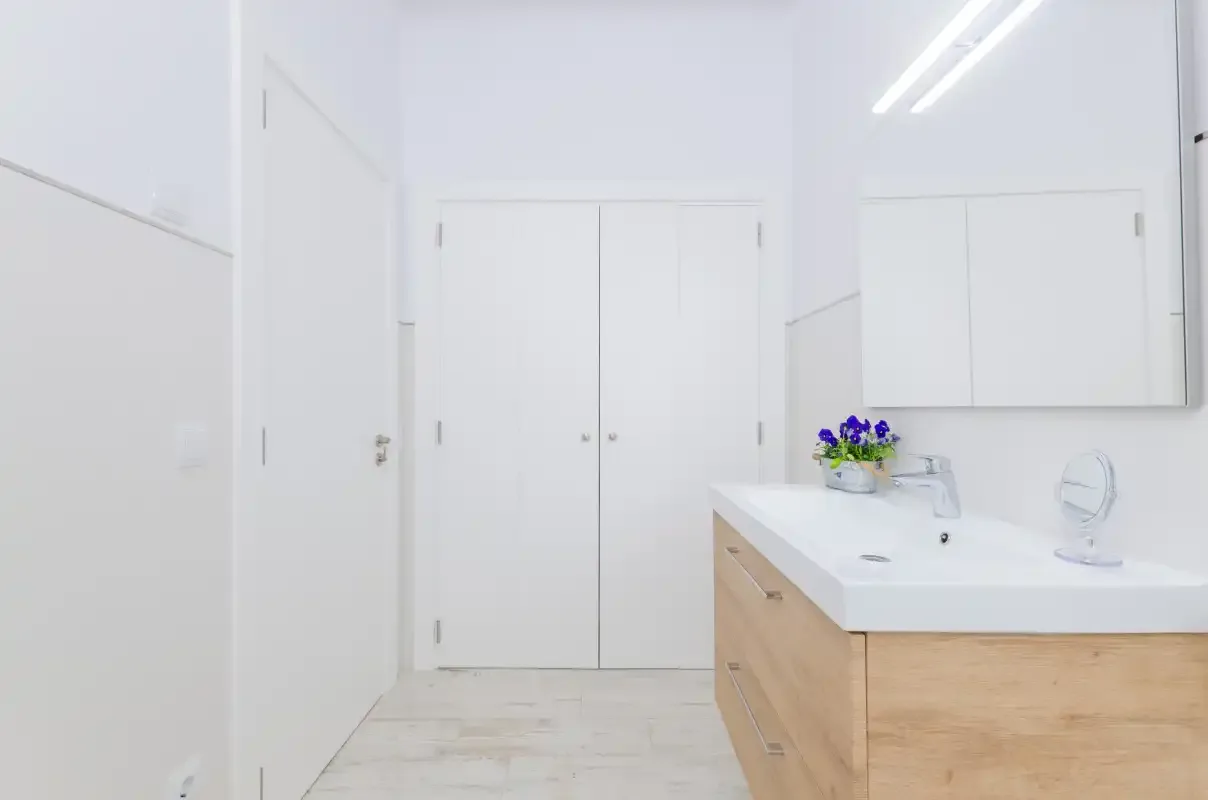 A bright bathroom with a white vanity, wood cabinetry, and flowers by the sink.