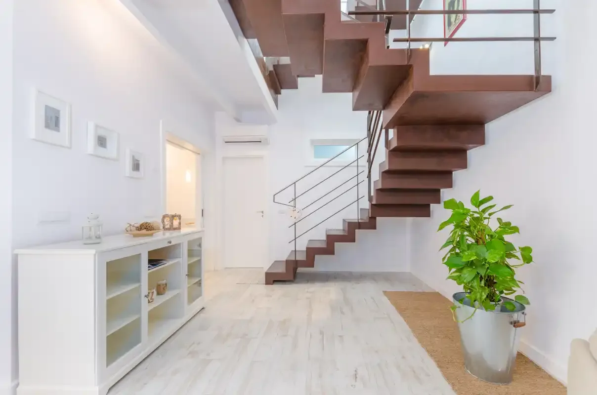 A bright interior hall with a floating staircase and a potted plant.