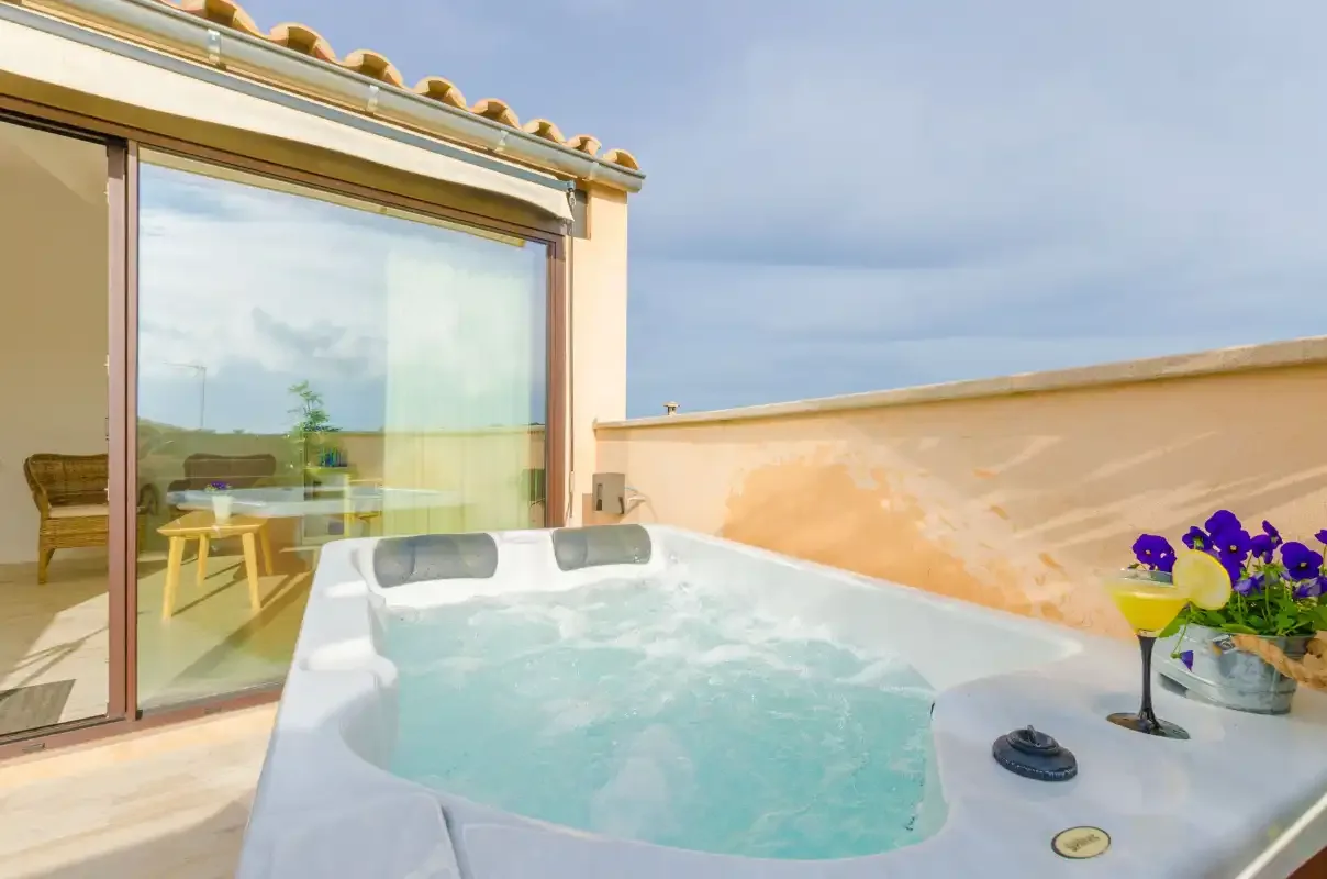 An outdoor hot tub sits beside a glass door and a potted plant.