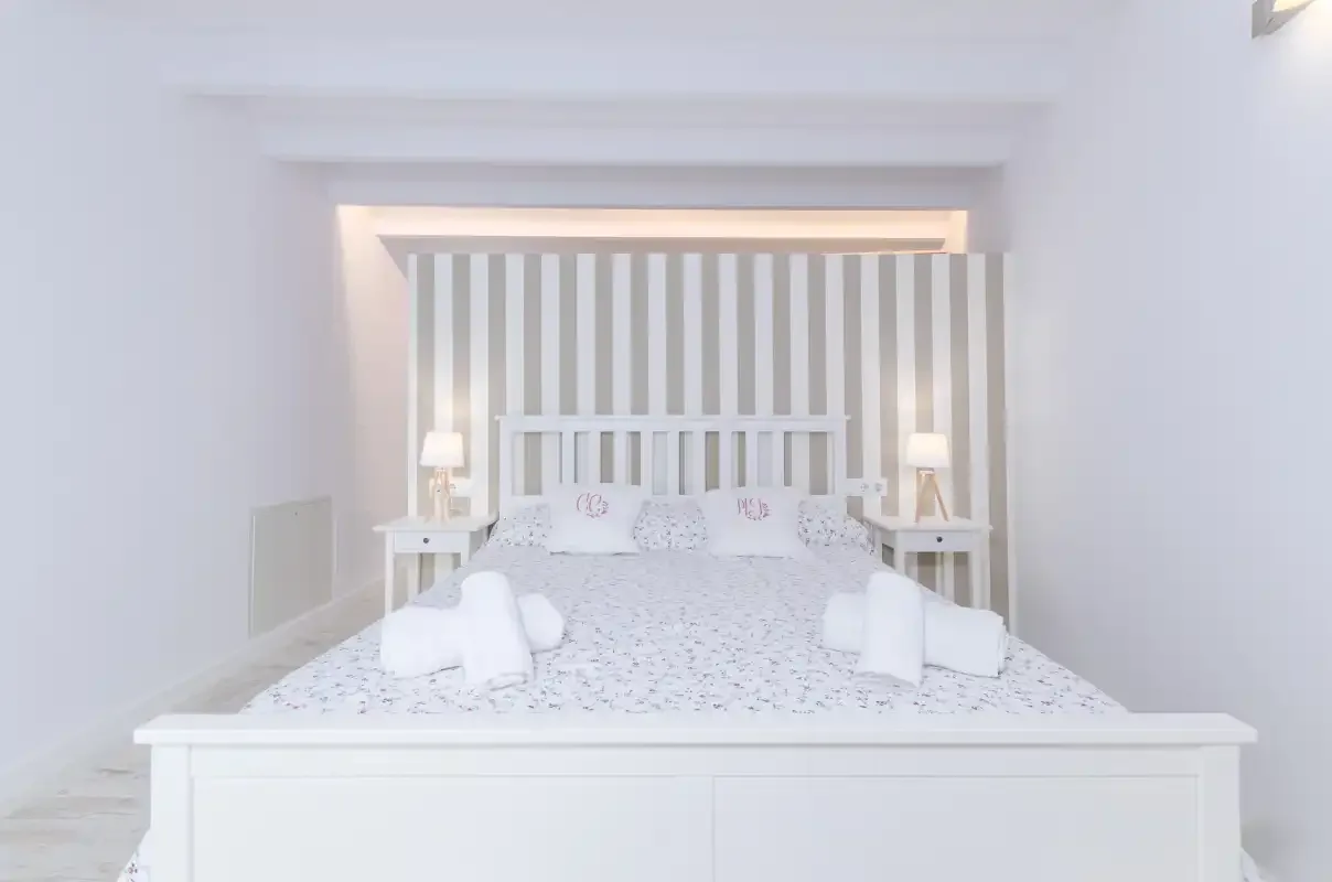 A bright bedroom with a bed set against a striped accent wall.