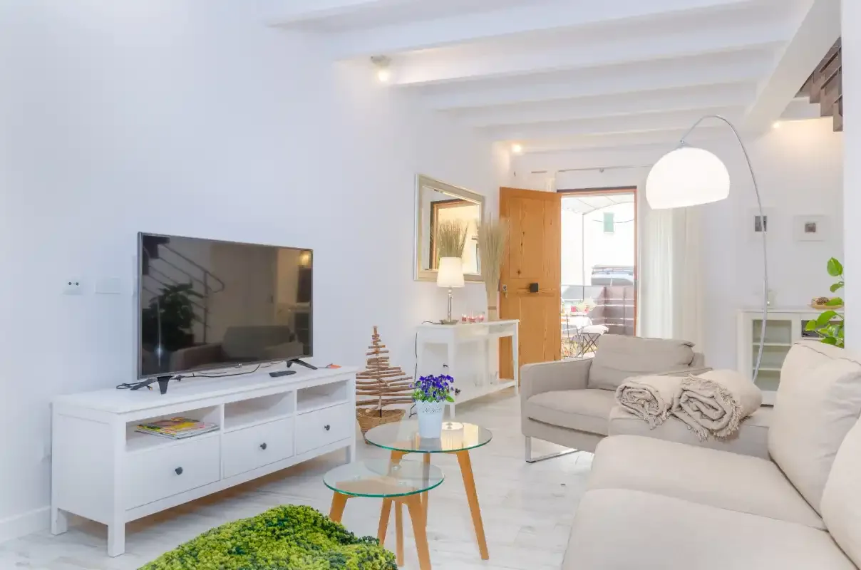 Bright living room with white seating, a television, and a glass coffee table.