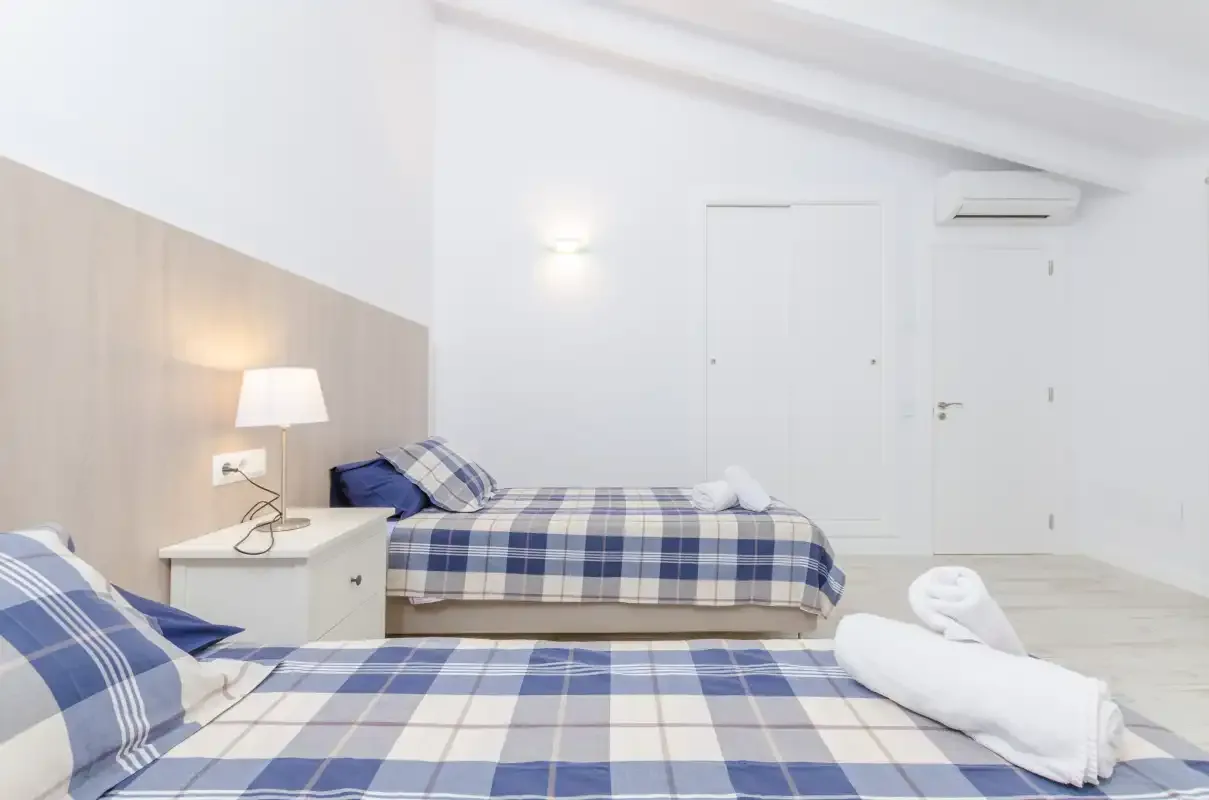 A bright bedroom with two beds dressed in blue plaid bedding.