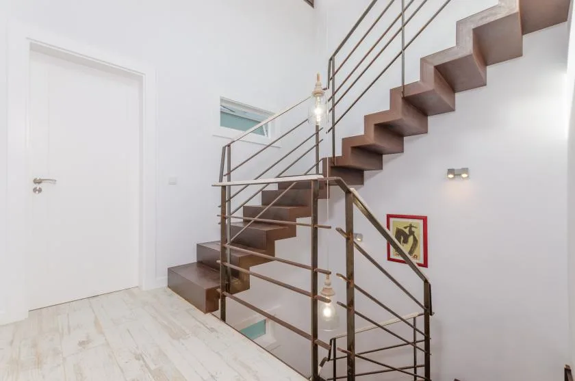 A bright stairwell with a floating staircase and metal railings.