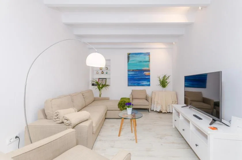 A bright living room with light seating, a coffee table, and a television.