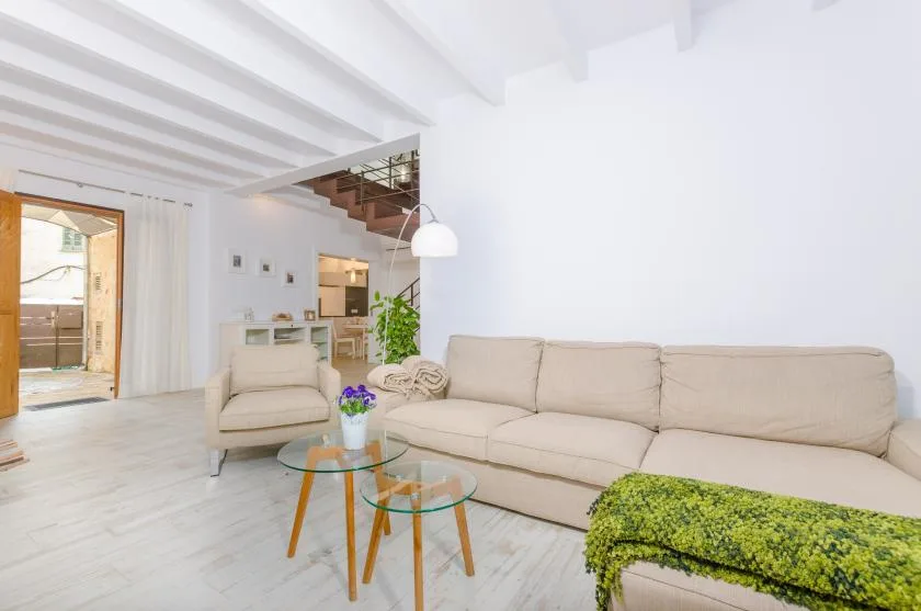 A bright living room with cream seating, glass tables, and an open doorway.