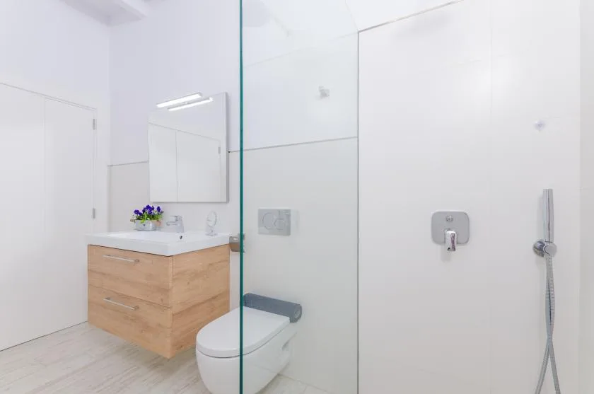 A bright bathroom with a wood-front vanity, toilet, and glass shower screen.