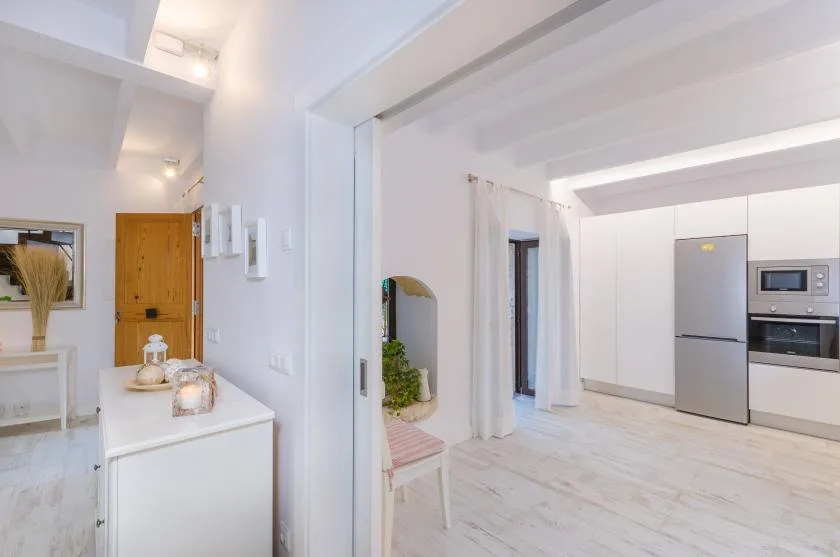 A bright interior hallway opens into a kitchen with white cabinetry and a refrigerator.