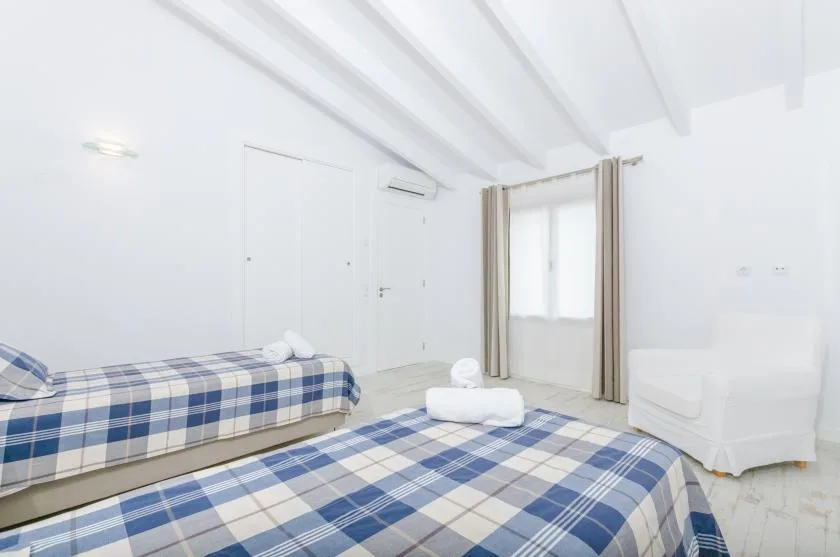 A bright bedroom with plaid bedding, a window, and a white armchair.