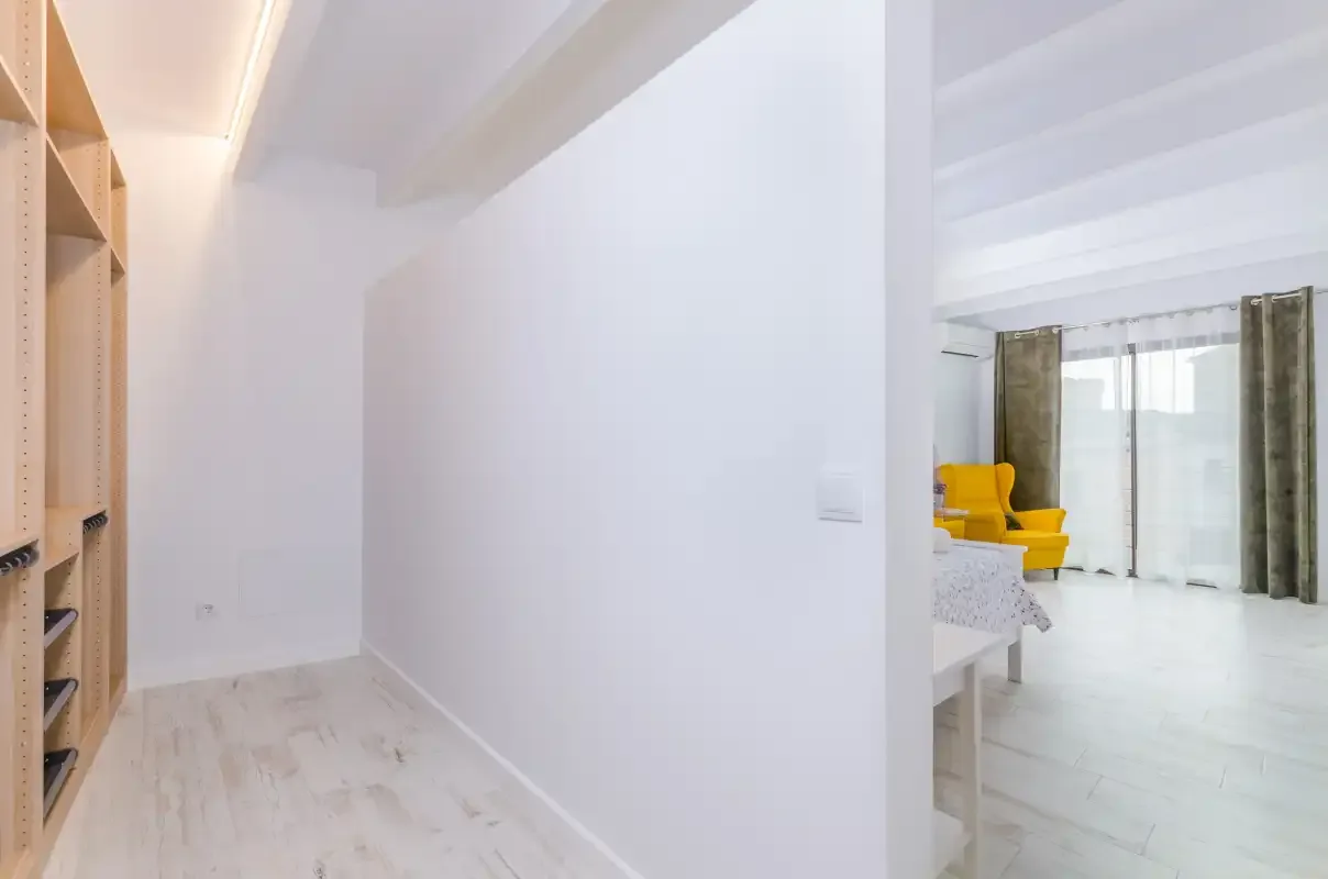 A bright hallway with built-in shelving opens into a room with yellow seating.