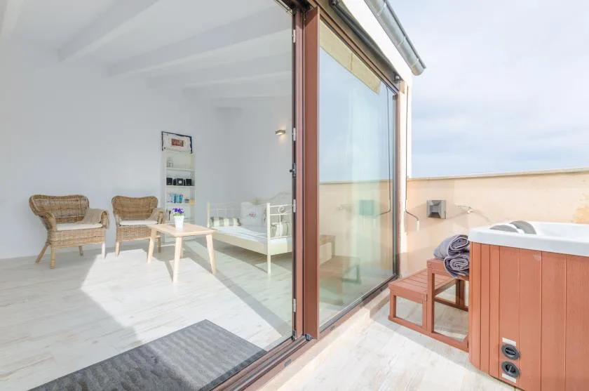 A bright room opens onto a small patio with seating and a hot tub.