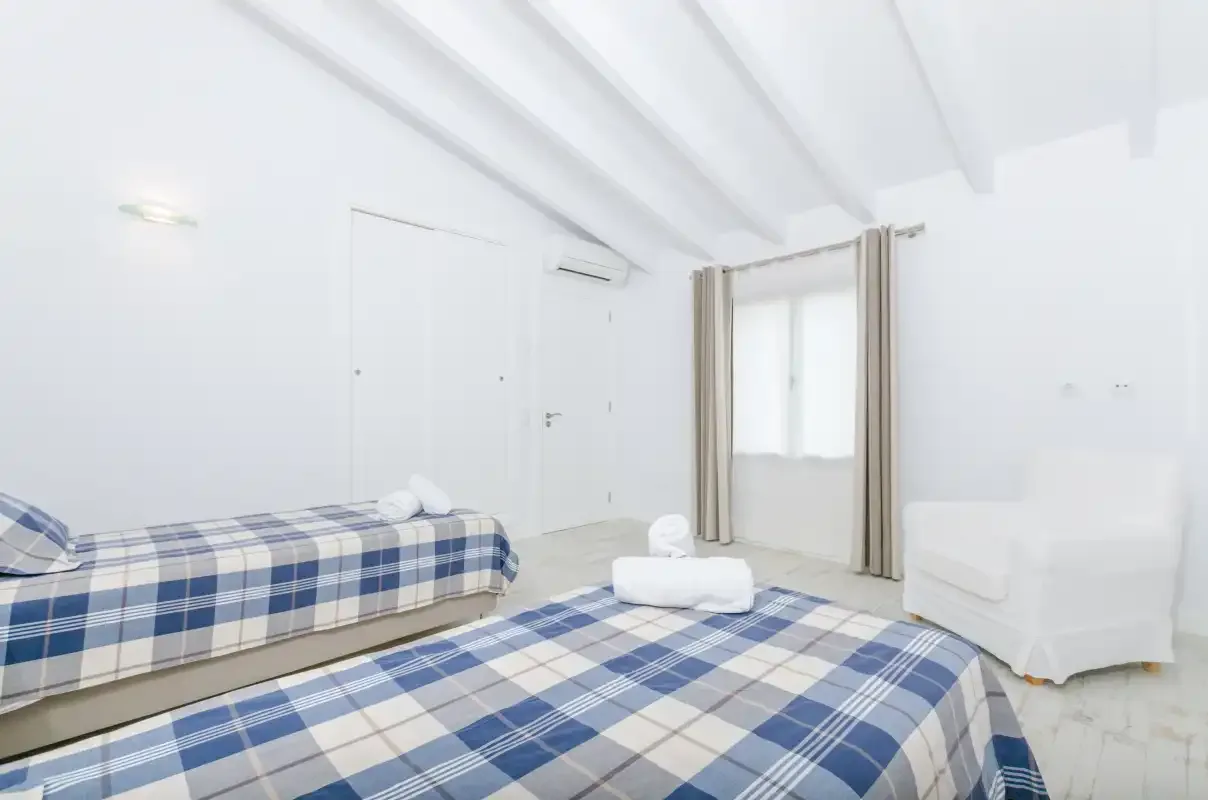 A bright bedroom with two beds covered in blue plaid bedding.