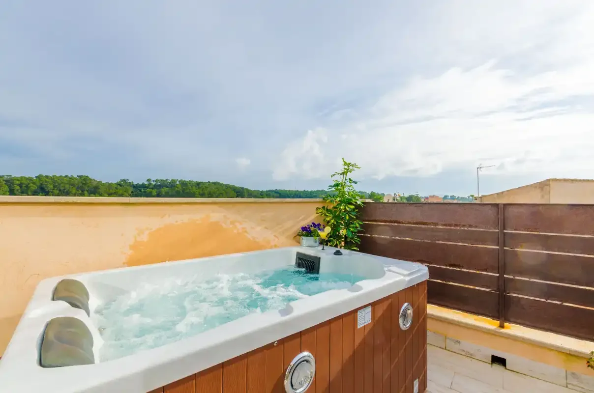 An outdoor hot tub sits on a tiled terrace beside a wooden privacy screen.