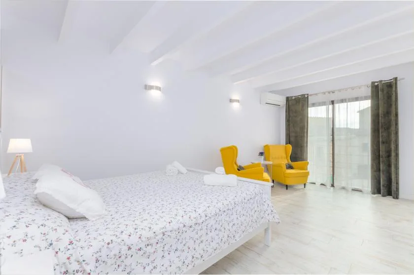 A bright bedroom with a floral bedspread and two yellow armchairs by the window.
