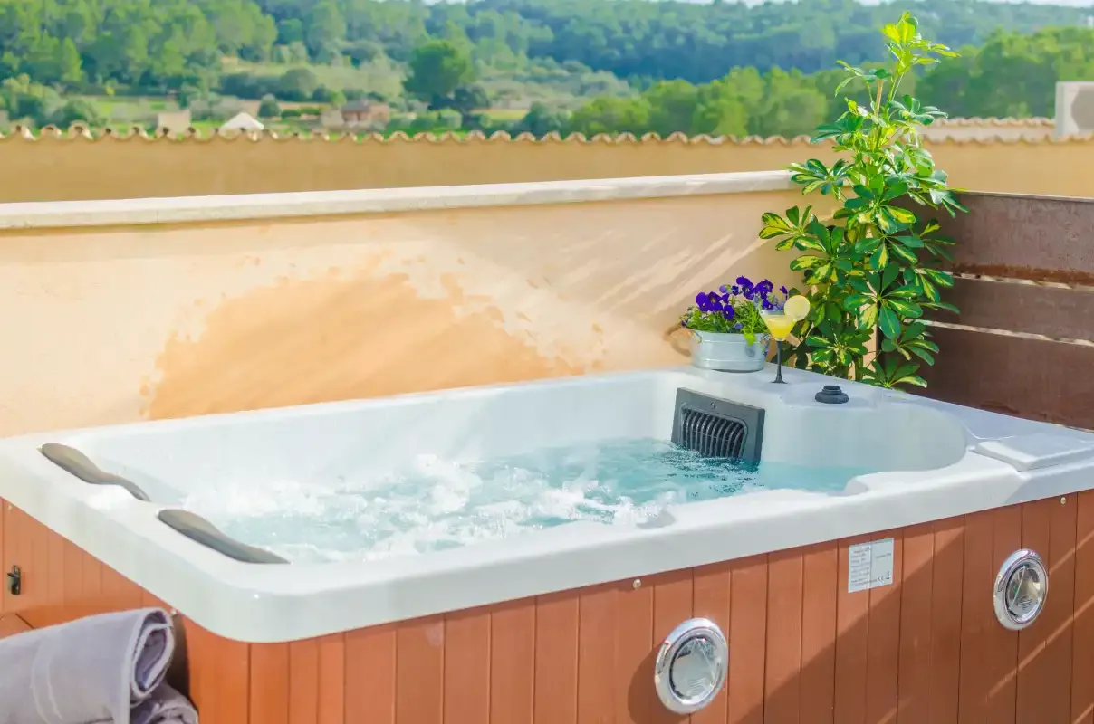 An outdoor hot tub sits beside a leafy plant on a terrace.