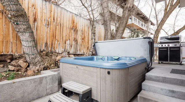 Una bañera de hidromasaje exterior está junto a un patio elevado y una parrilla.