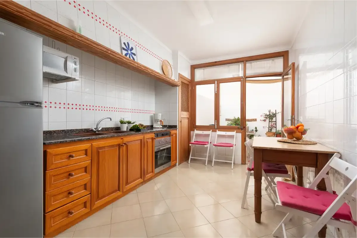 A tiled kitchen with wooden cabinets opens onto a dining area by the windows.