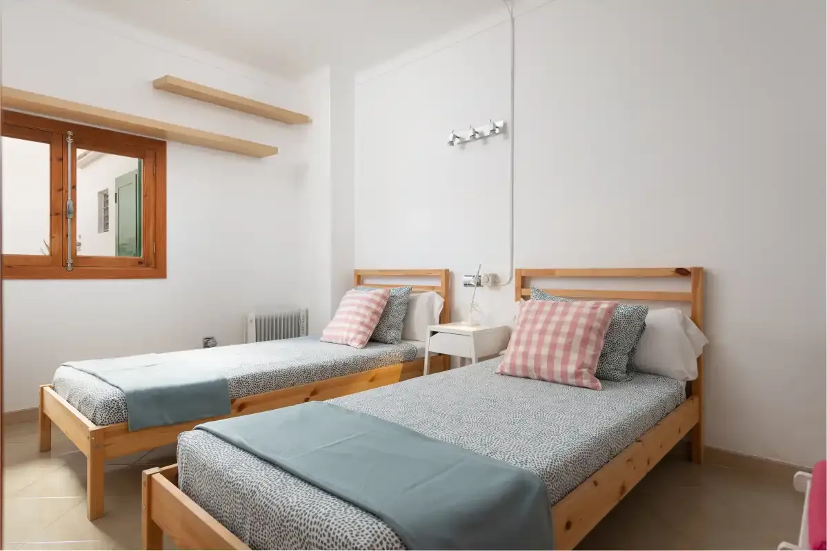 A bright bedroom with two single beds and a window.