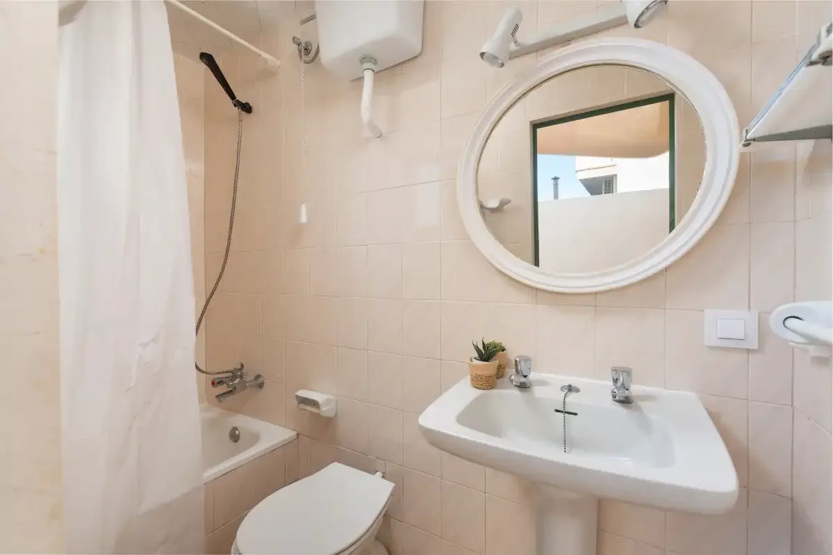A tiled bathroom with a sink, oval mirror, and shower curtain.